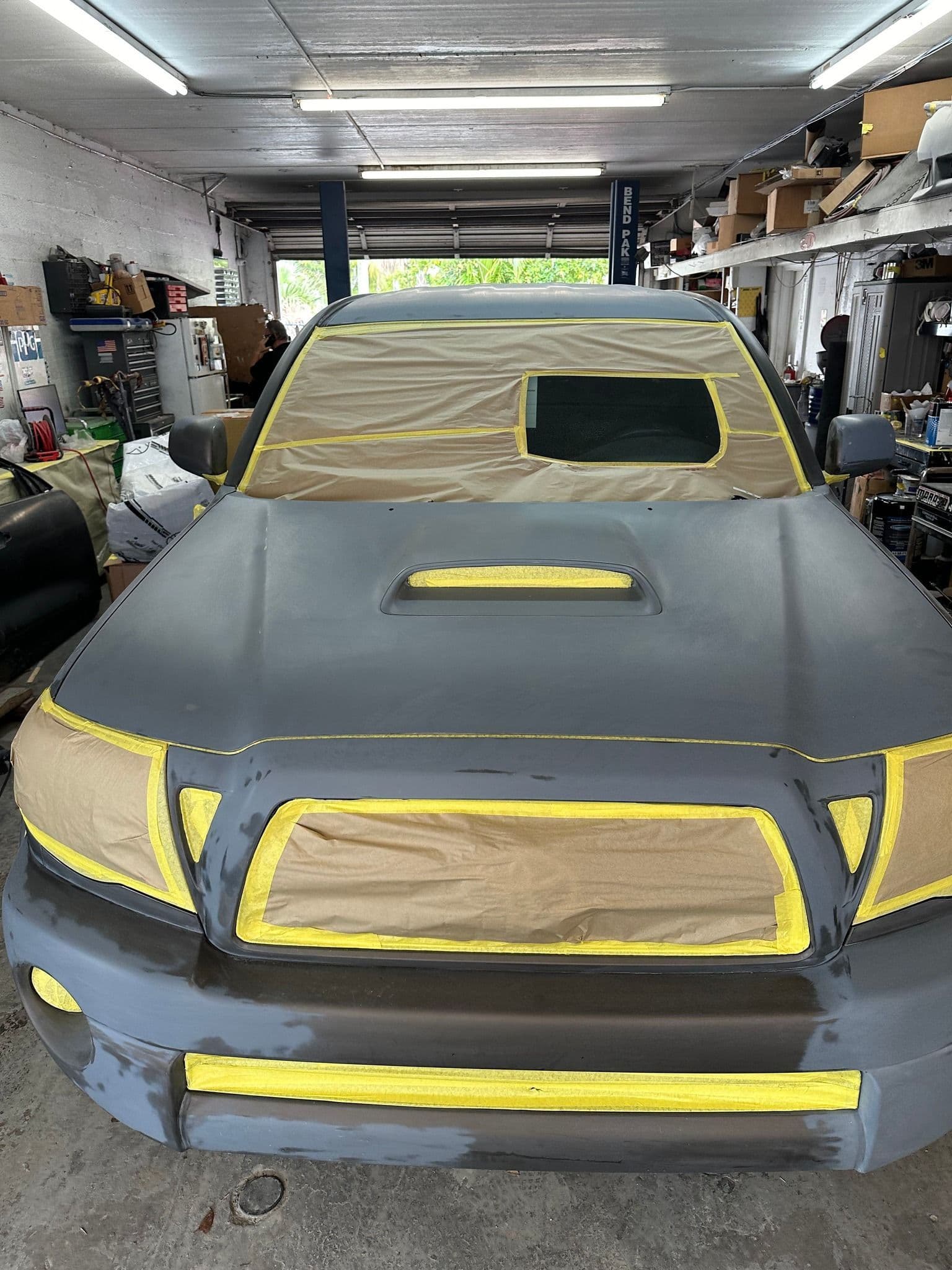 Compact pickup masked with yellow tape for paint inside the shop